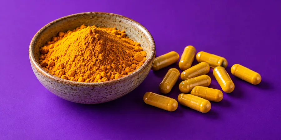 Bol de poudre de curcuma posé à côté de gélules jaunes sans marque sur un fond violet vif