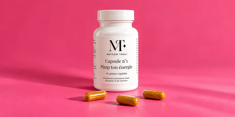 Flacon de la Capsule n°1 de Maison Thali posé à côté de quelques gélules, sur un fond rose vif